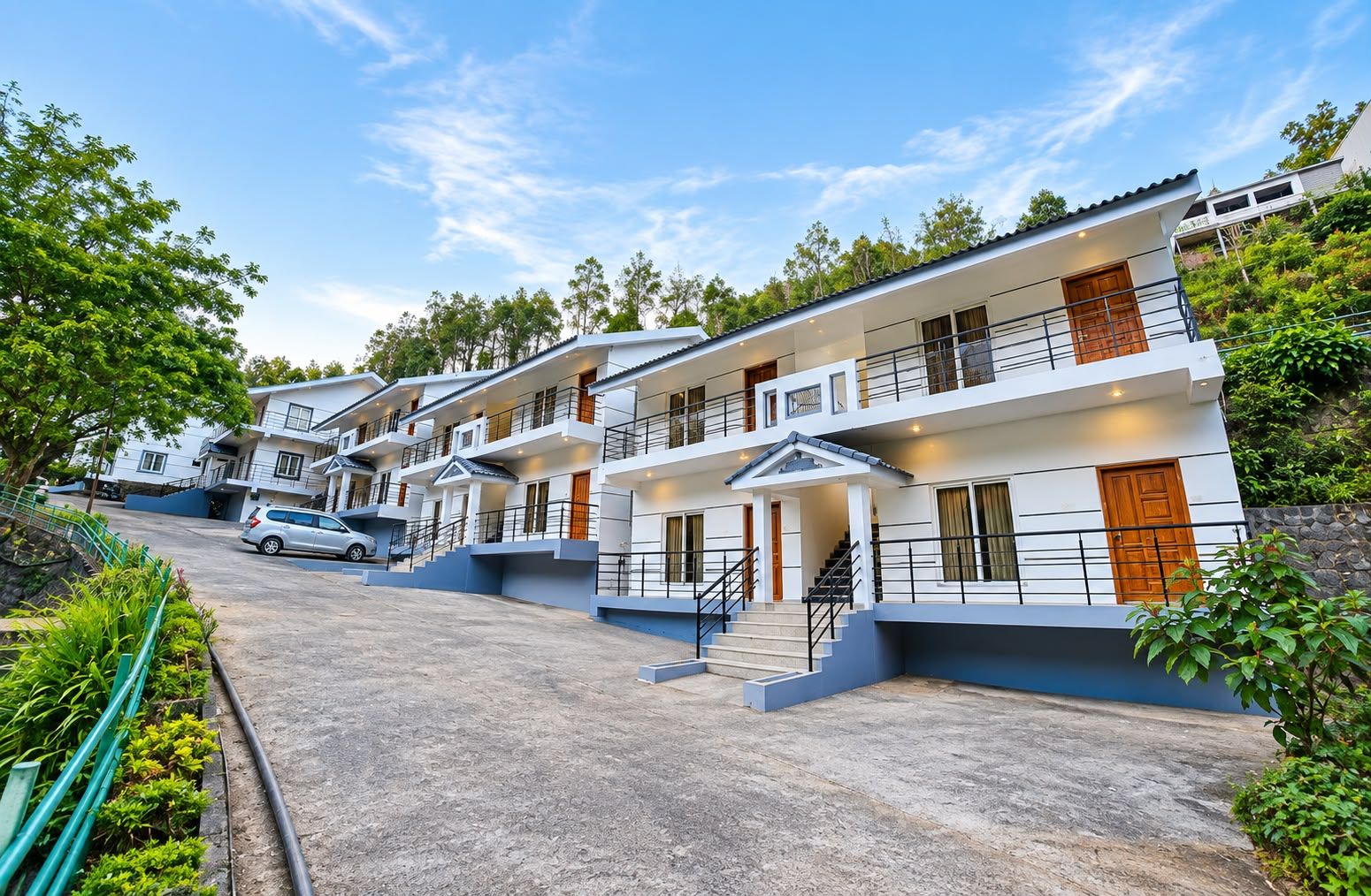 A row of modern, multi-story buildings with balconies, a car parked in front, and a clear sky.