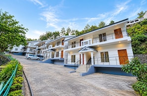 A row of modern, multi-story buildings with balconies, a car parked in front, and a clear sky. - Anglo French Resort Yercaud (Yercaud)