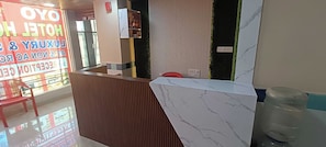 A hotel reception area with a wooden reception desk, a water dispenser, and a red chair. - Hotel O Holiday Inn (Hyderabad)