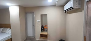 A small, compact room with a single bed, a desk with a chair, and a built-in air conditioning unit. - Hotel O Holiday Inn (Hyderabad)