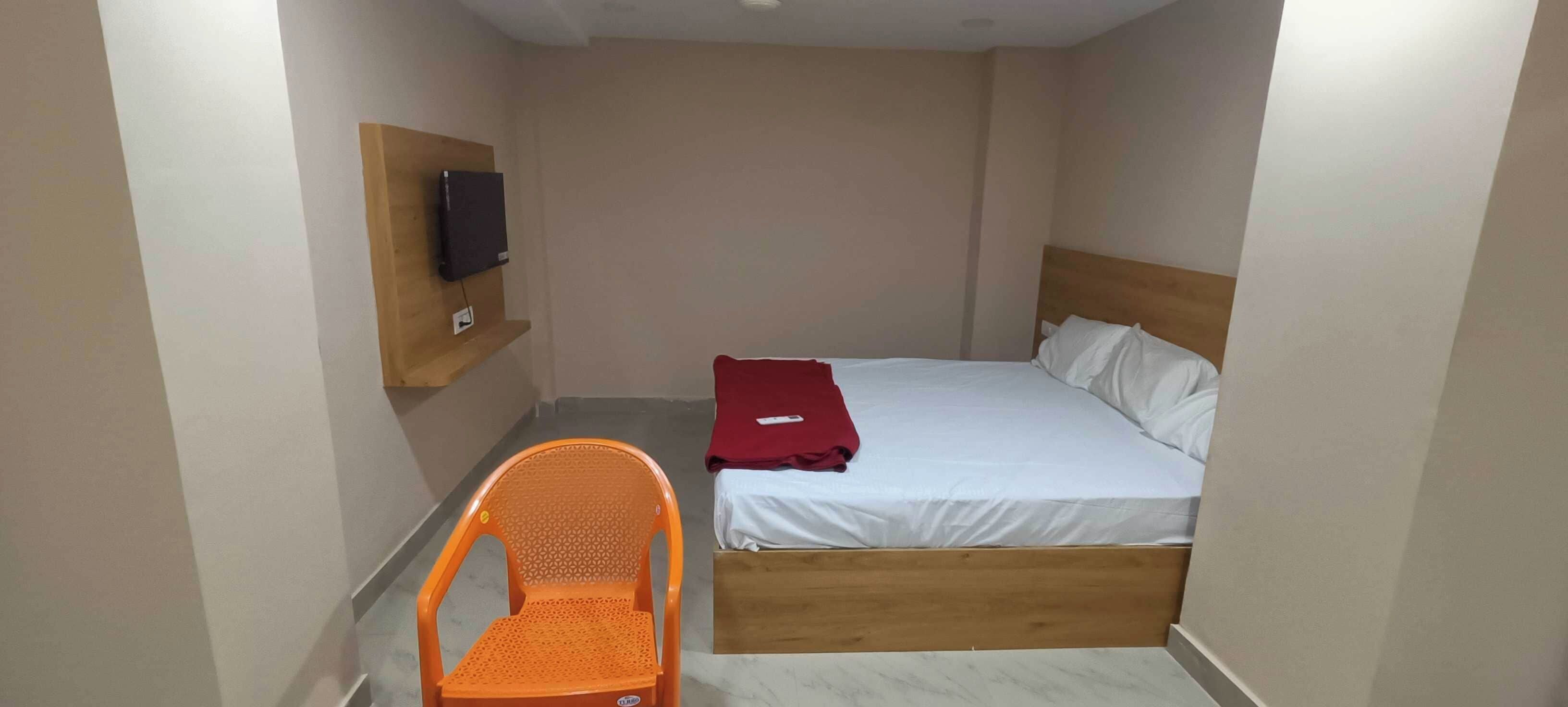 A small room with a single bed, a wooden headboard, a wall-mounted TV, and a single orange chair.