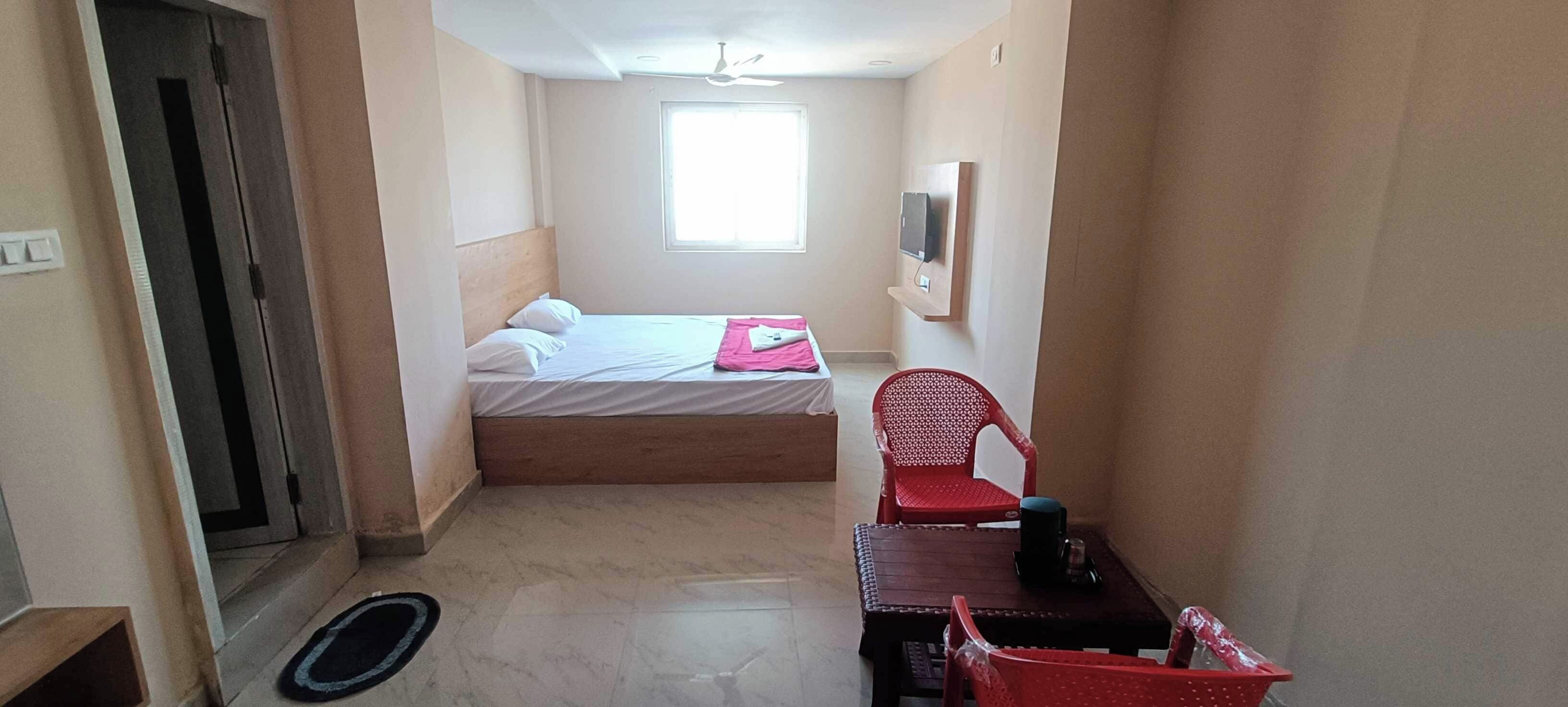 Un pasillo estrecho que conduce a un dormitorio con cama, una silla, una mesa y un ventanal.