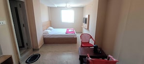 A narrow hallway leading to a bedroom with a bed, a chair, a table, and a window. - Hotel O Holiday Inn (Hyderabad)