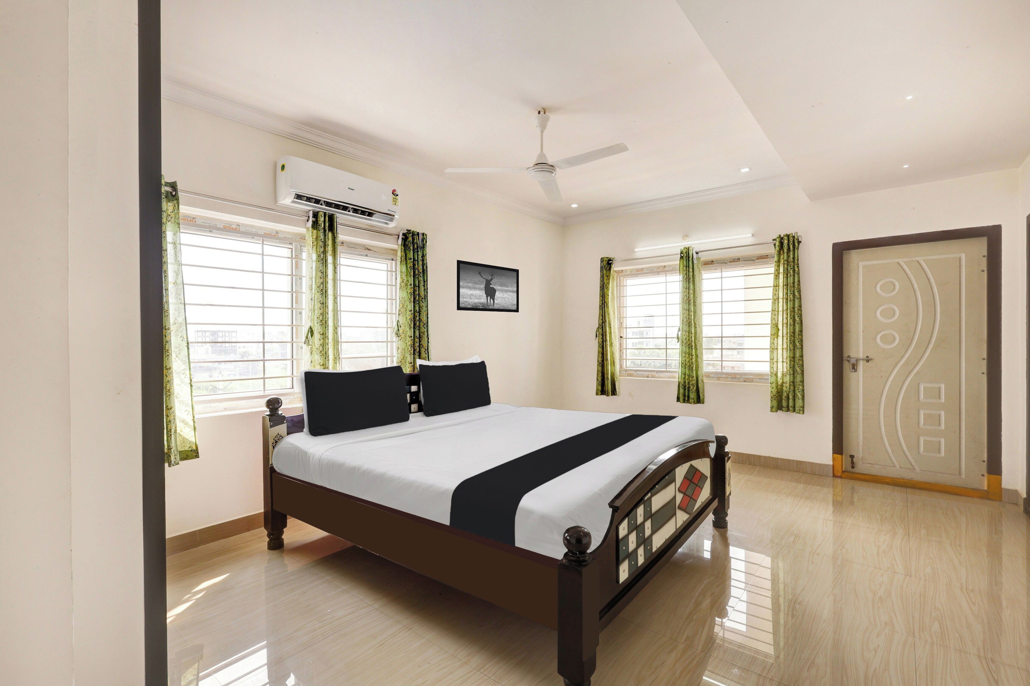 A bedroom with a bed, air conditioning unit, ceiling fan, windows with curtains, and a door.