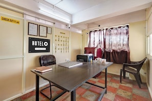 Camera d'albergo con cartello di check-out, una scrivania con un portatile, una sedia, una finestra con tende e un muro con numeri di stanza e certificati.