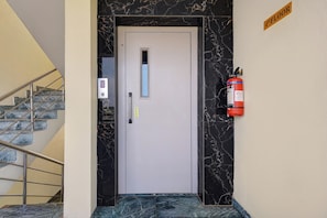 Entrada de hotel con una escalera de mármol, un panel de control digital para el ascensor y un extintor de incendios en la pared.