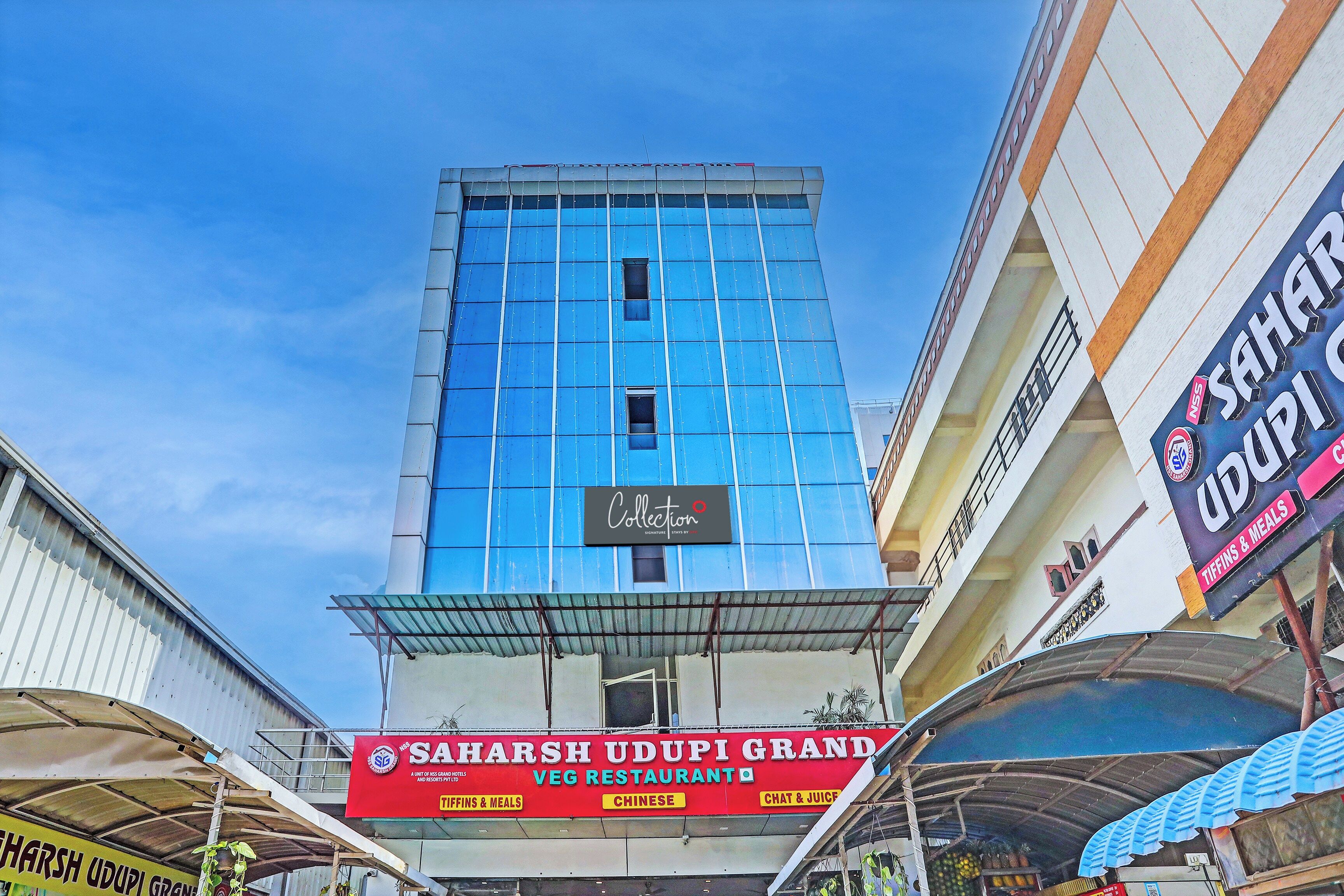 Hotel amb façana blava destacada i indicadors per 'Saharsh Udupi Grand' i 'Veg Restaurant'.