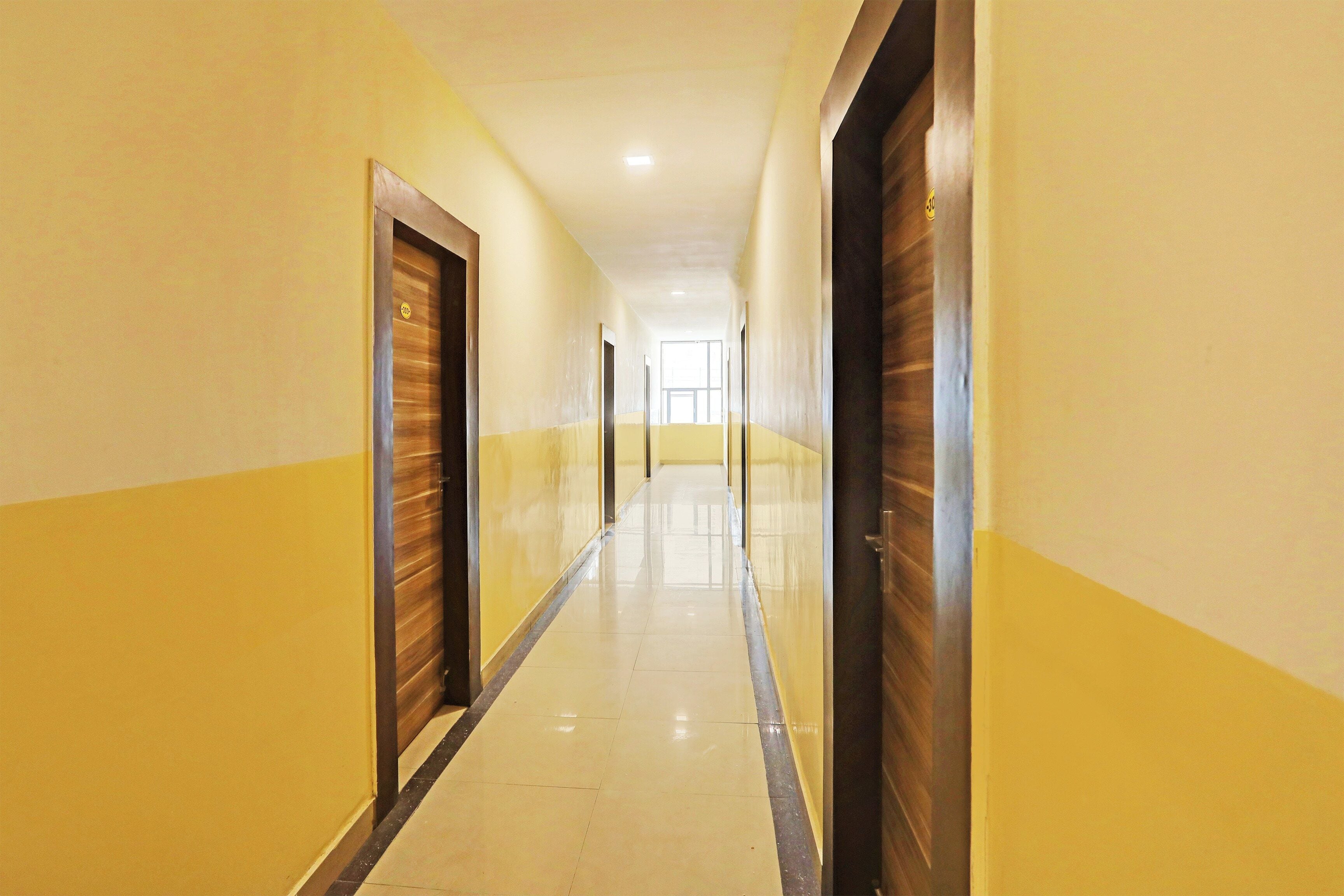 A long, narrow hallway with doors on both sides, leading to a bright room at the end.