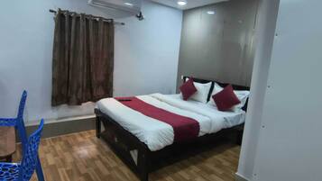 Un dormitorio con cama, ventana con cortinas, una silla azul y suelo de madera.
