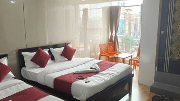 Habitación de hotel con dos camas, un balcón con sillas naranjas y vistas a la ciudad.