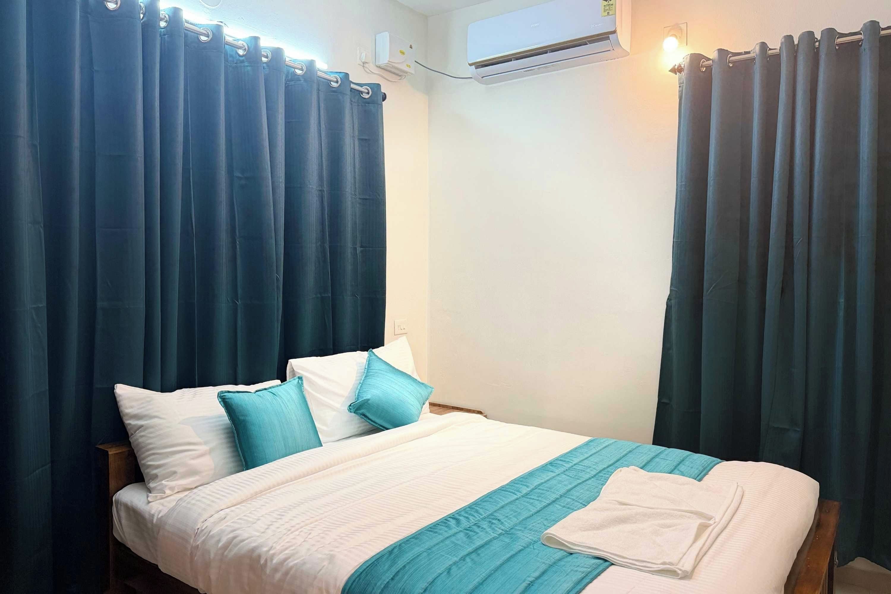 Una habitación de hotel con cama, cortinas, aire acondicionado y una lámpara de pared.