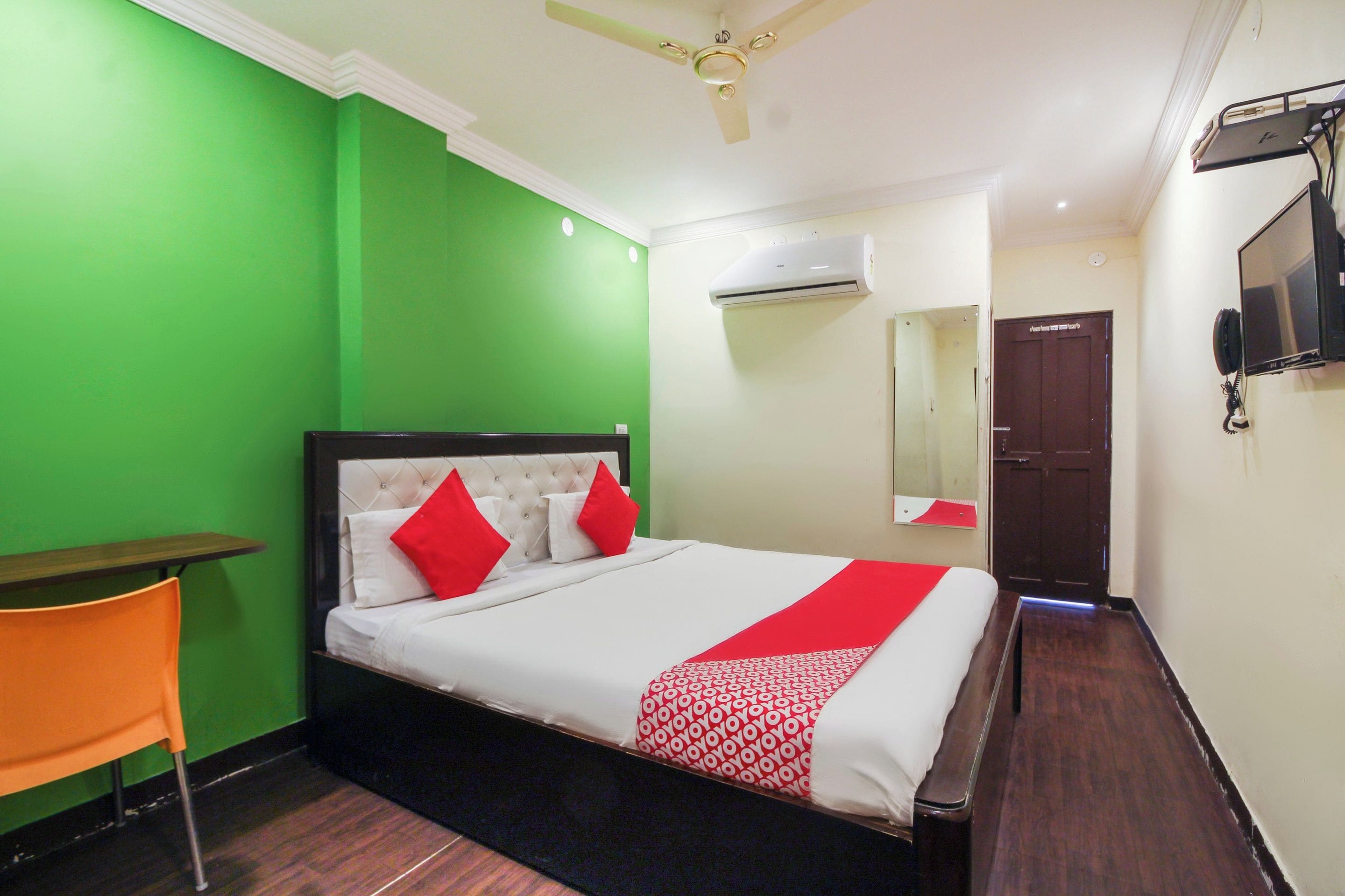 A hotel room with a bed, a desk, a chair, a television, and an air conditioning unit.