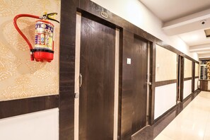 Passadís d'hotel amb portes de fusta fosca, un extintor fixat a la paret i un senyal amb un número sobre les portes.