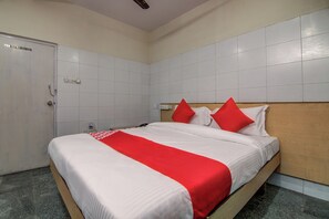 Una habitación de hotel con una cama, cabecera de madera, pared blanca, una puerta y un interruptor de luz.