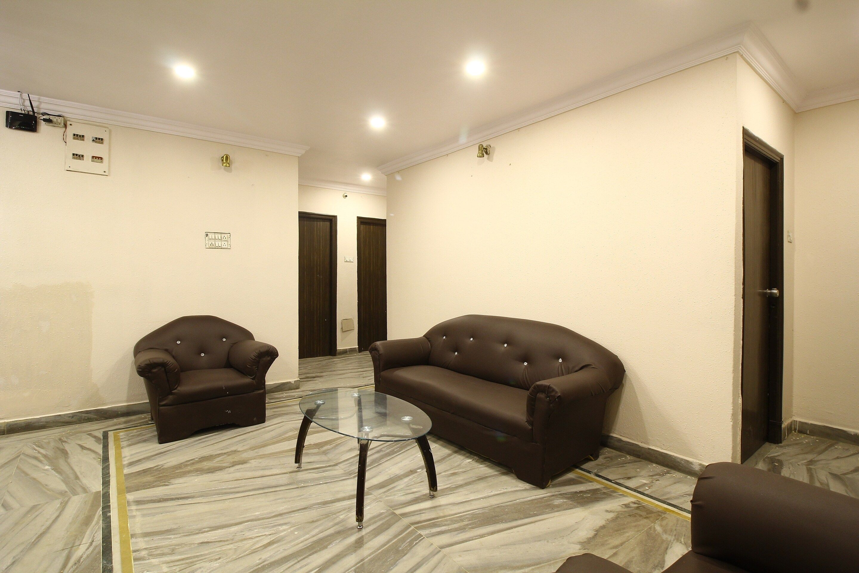Una habitación con dos sofás marrones, una mesa de centro de vidrio y suelo de mármol.