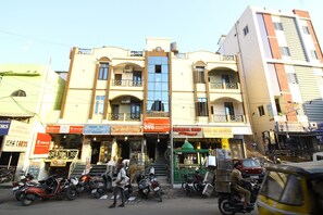 Un edificio de varios pisos con locales comerciales en la planta baja, incluyendo una tienda con un letrero que dice 'SRI BATCHA CARDS' y otra con el letrero 'SRI SANGEET STORE'.
