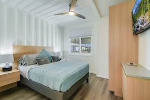 A bedroom with a bed, nightstands, a ceiling fan, a window with a view, and a mounted TV.