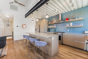 A modern kitchen with a central island, bar stools, a stove, and blue tiled backsplash.