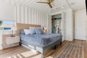 A modern bedroom with a bed, bedside table, lamp, ceiling fan, and built-in wardrobe. - Red Dawn: Container Home w/ Heated Plunge Pool, Walk to Beach, Sleeps 10 (Port Aransas)