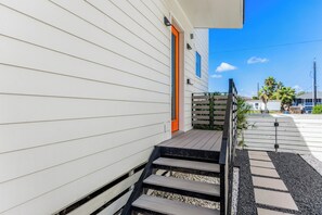 Um imóvel residencial com varanda de madeira, degraus que levam a uma porta e céu claro.