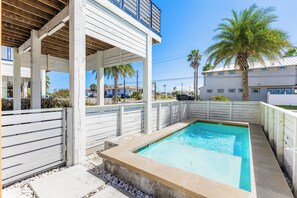 A residential pool area with a concrete deck, a wooden fence, and a palm tree. - Orange Sunset: Container Home w/ Heated Plunge Pool, Near Beach, Sleeps 10 (Port Aransas)