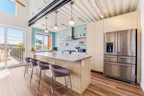 A modern kitchen with a large island, bar stools, stainless steel appliances, and a view to the outside. - Orange Sunset: Container Home w/ Heated Plunge Pool, Near Beach, Sleeps 10 (Port Aransas)