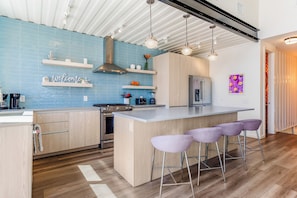 A modern kitchen with a central island, bar stools, and a blue backsplash.