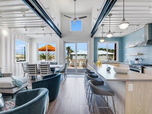 A modern kitchen with a large island, bar stools, and a dining area with a view. - Orange Sunset: Container Home w/ Heated Plunge Pool, Near Beach, Sleeps 10 (Port Aransas)