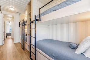 A bunk bed room with a wooden floor, a small desk, and a window.