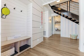 A modern interior with a wooden floor, a staircase, and a shoe rack with a sign. - Orange Sunset: Container Home w/ Heated Plunge Pool, Near Beach, Sleeps 10 (Port Aransas)