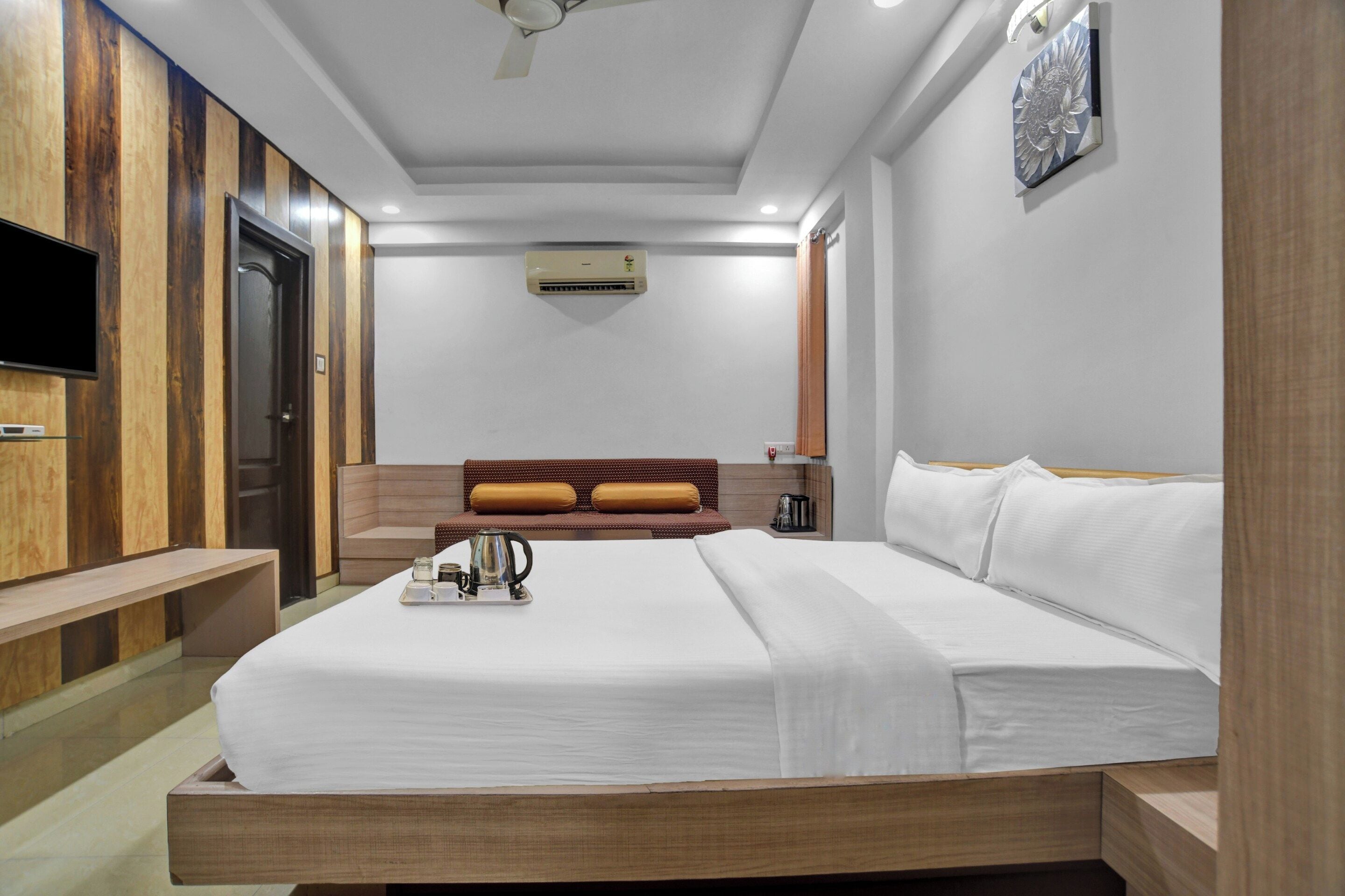 A hotel room with a bed, a TV, a coffee table, and a wall-mounted air conditioner.