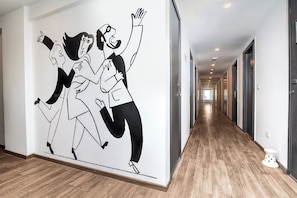 Un pasillo con un gran mural en blanco y negro de bailarines, piso de madera y vista a una habitación con una puerta al final.