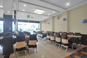 Un salón de banquetes con filas de mesas y sillas, luces en el techo y globos decorativos.