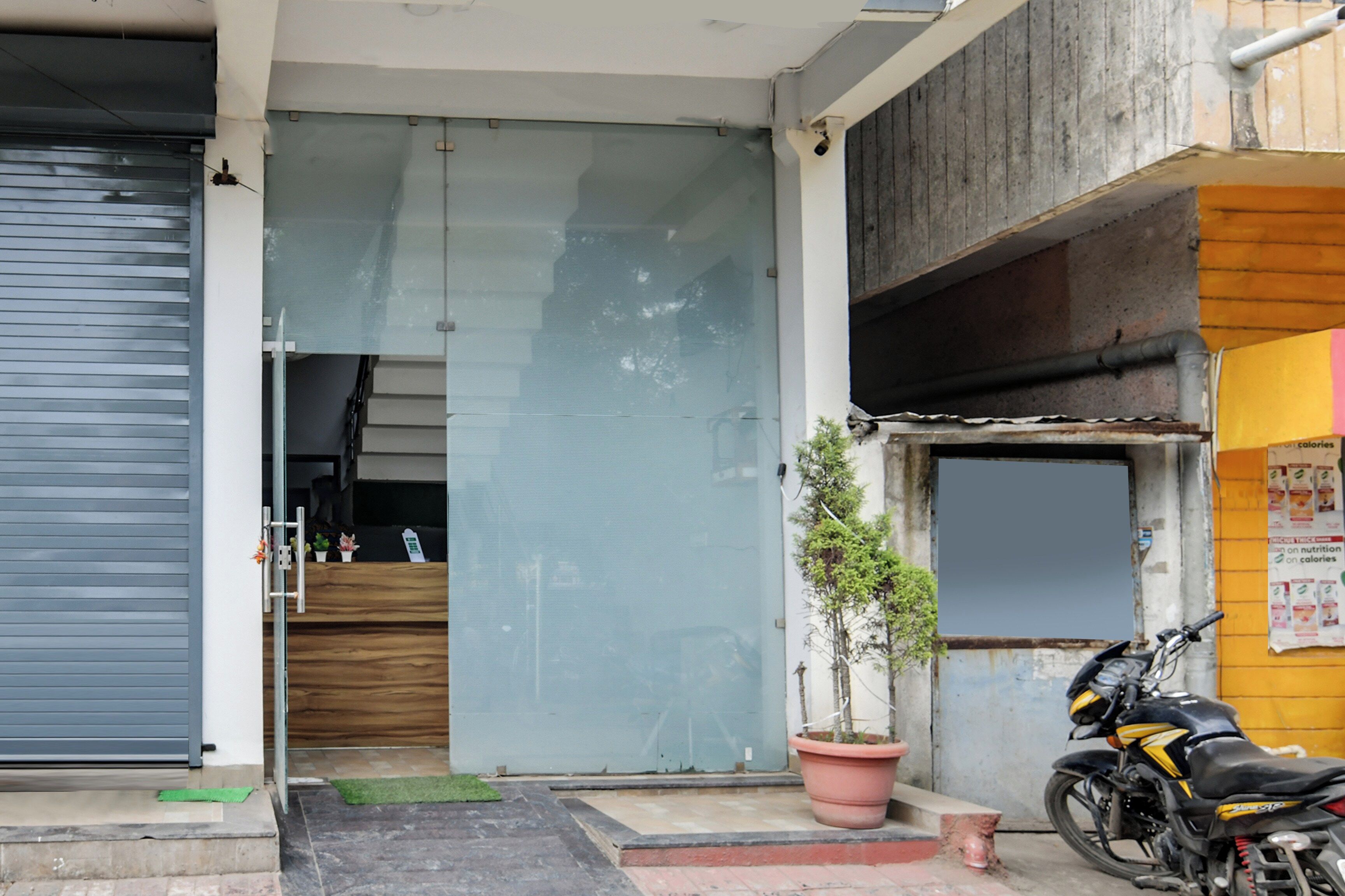 A building entrance with a closed shutter, a potted plant, and a motorcycle parked outside.