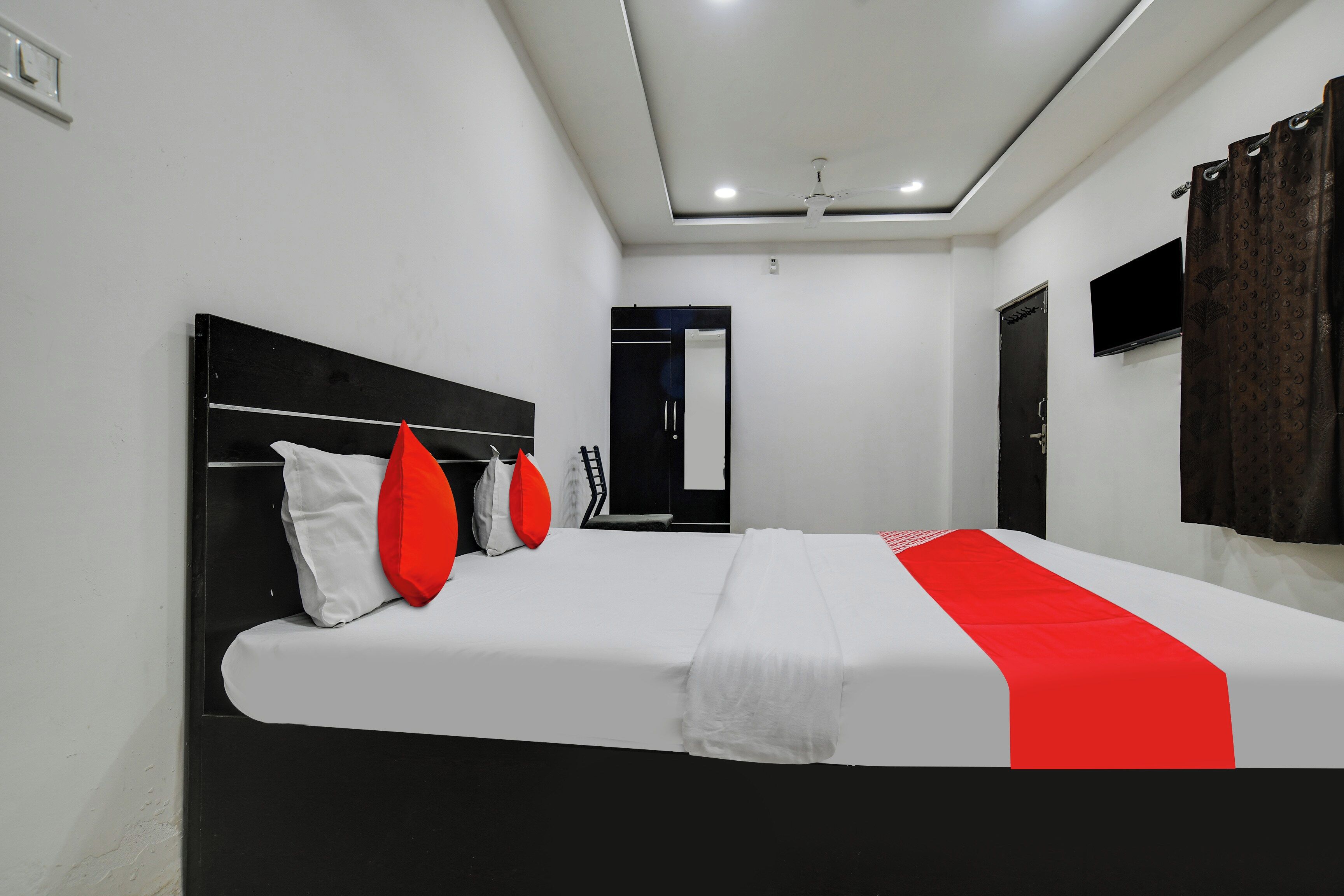 A hotel room with a bed, a flat-screen TV mounted on the wall, and a ceiling fan.