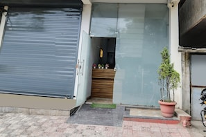 Un comercio cerrado con un cerrojo metálico, un mostrador de madera en el interior y una planta en maceta en el exterior.