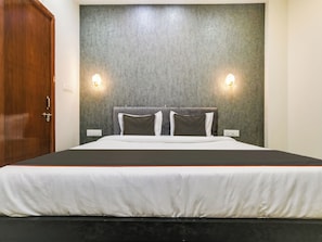 A hotel room with a bed, a wooden door, and two wall-mounted light fixtures. - Hotel O by OYO Iconic Stay (Indore)