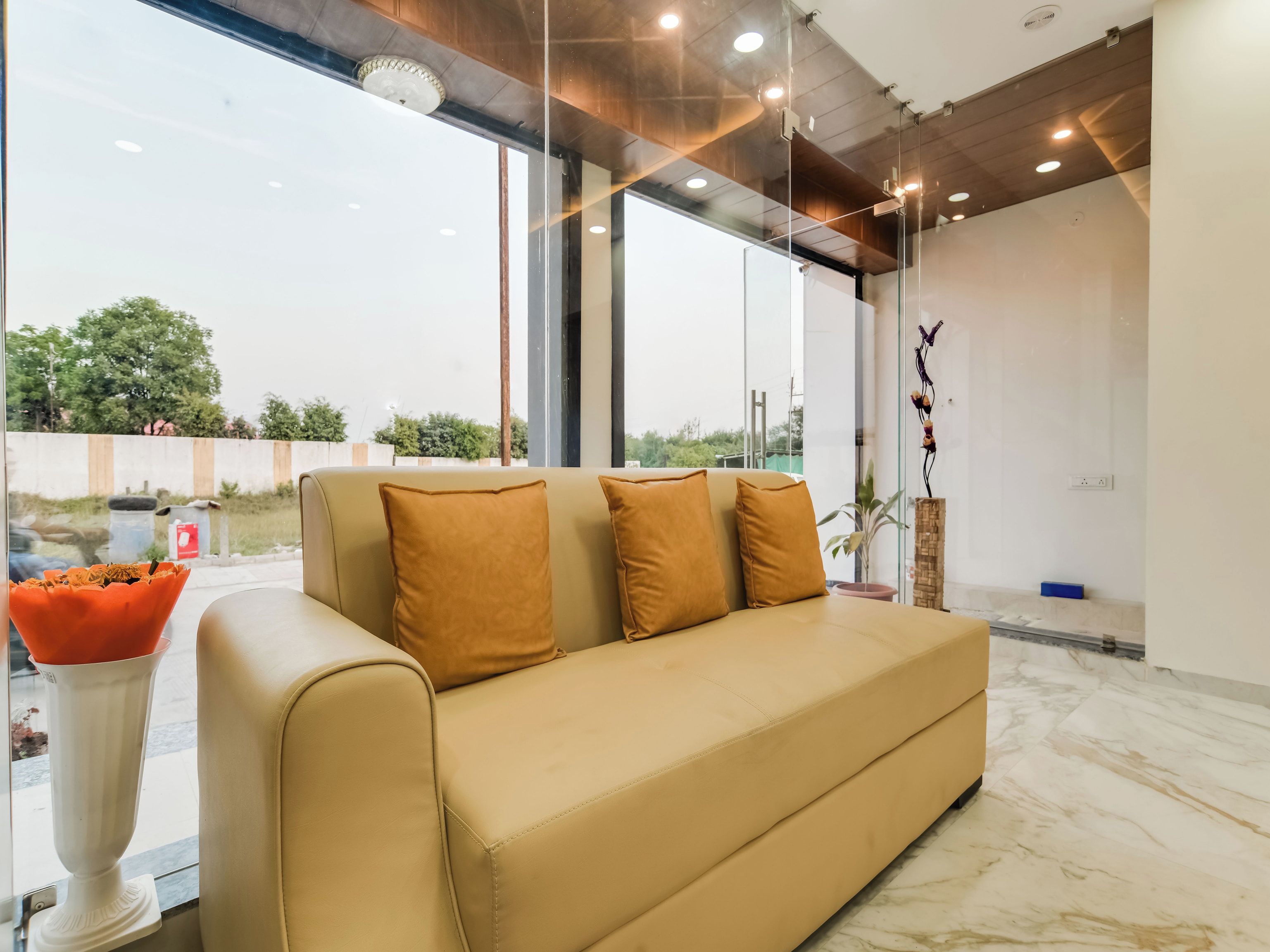 A modern interior with a sofa, a vase with dried flowers, and a view through a glass wall.