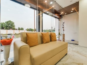 Un interior moderno con un sofá, un jarrón con flores secas y vistas a través de un muro de cristal.