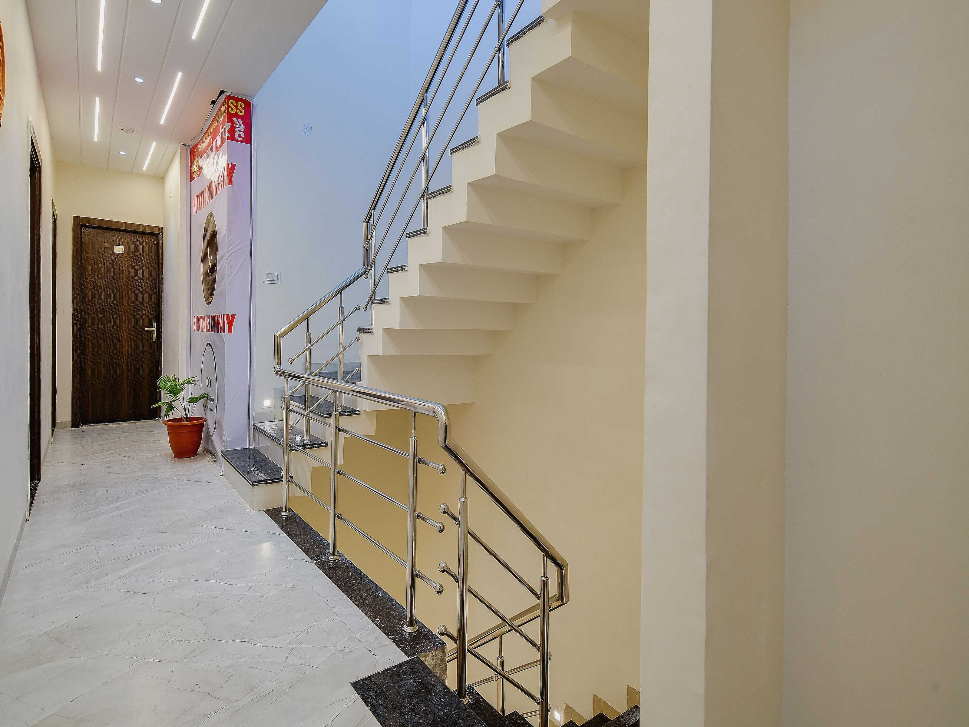 A hotel hallway with a marble floor, a wooden door, a staircase with metal railings, and a potted plant.
