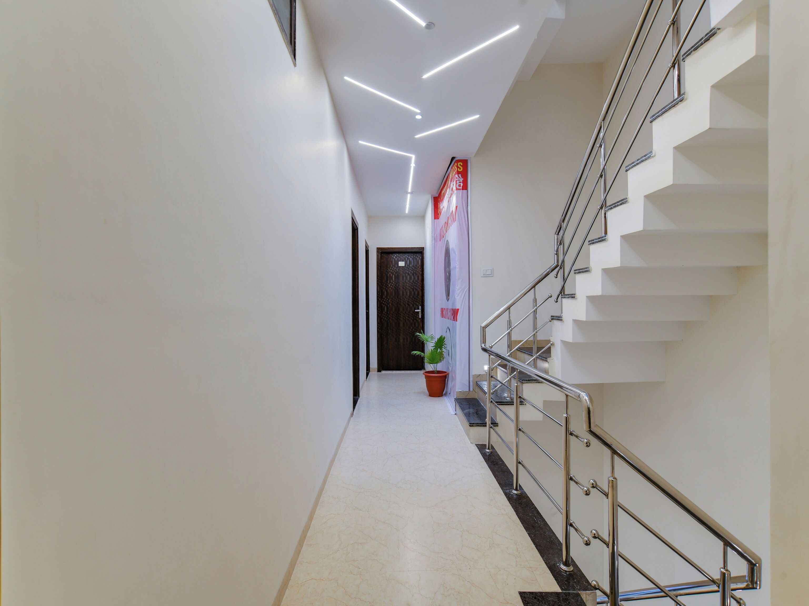 A modern hotel hallway with a staircase, a potted plant, and a sign on the wall.