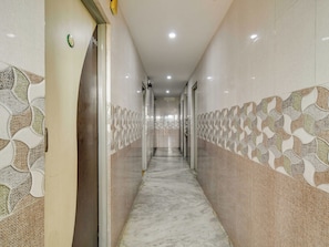A corridor with patterned walls and a marble floor, leading to a door with a number plate. - Hotel O BR Greens (Indore)