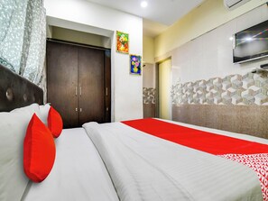 A hotel room with a bed, a wardrobe, a television, and decorative wall tiles. - Hotel O BR Greens (Indore)