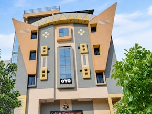 A modern building with a unique geometric facade, a prominent central entrance, and a sign indicating a café and restaurant. - Hotel O BR Greens (Indore)