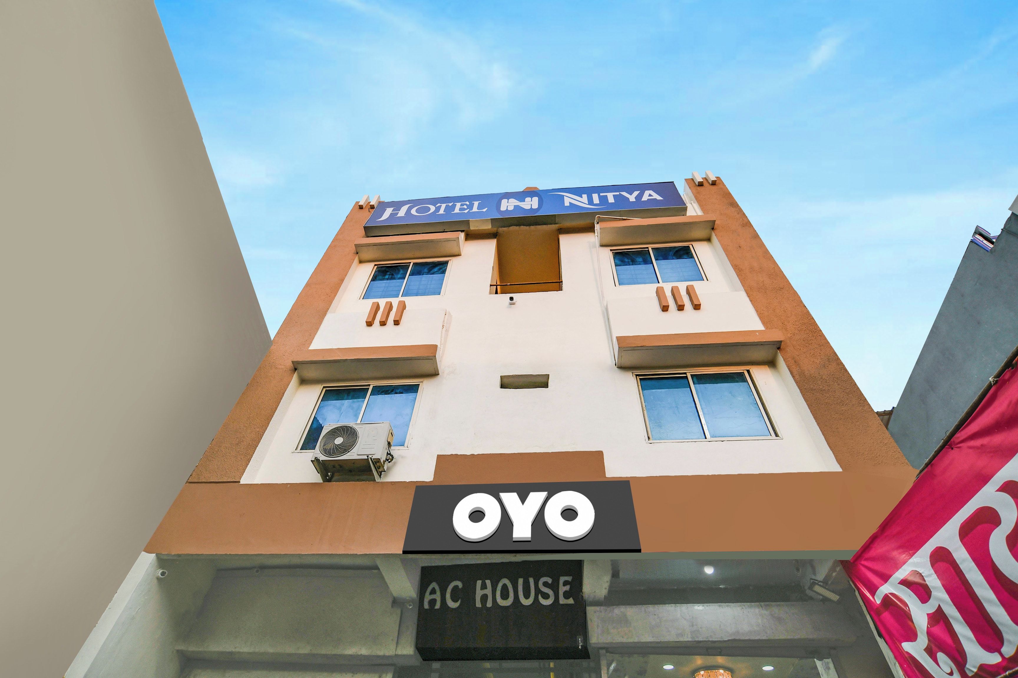 Un edificio de hotel con un cartel que indica 'HOTEL NITYA' y 'AC HOUSE', señalando la presencia de un equipo de aire acondicionado.