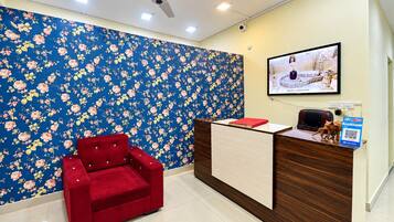 Un área de recepción con papel tapiz floral, una silla roja, un mostrador de madera, un televisor montado en la pared y un letrero de PayApp.