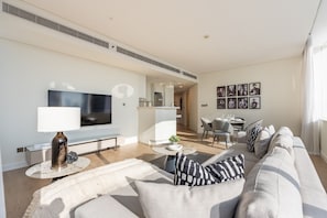 A modern living room with a sofa, a TV, and a dining area with chairs and a table. - High-Floor 2BR with City Views and Near Dubai's Major Landmarks, Sky Gardens (Dubai)