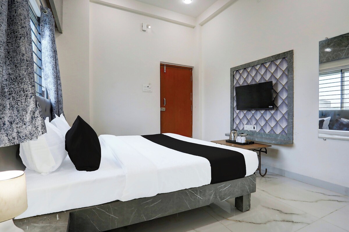 A hotel room with a bed, a television mounted on a wall, a door, and a window with blinds.