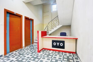 A reception desk with a sign that reads 'OYO' in a hallway with patterned floor tiles and two wooden doors. - Hotel O Grand Embassy (Indore)