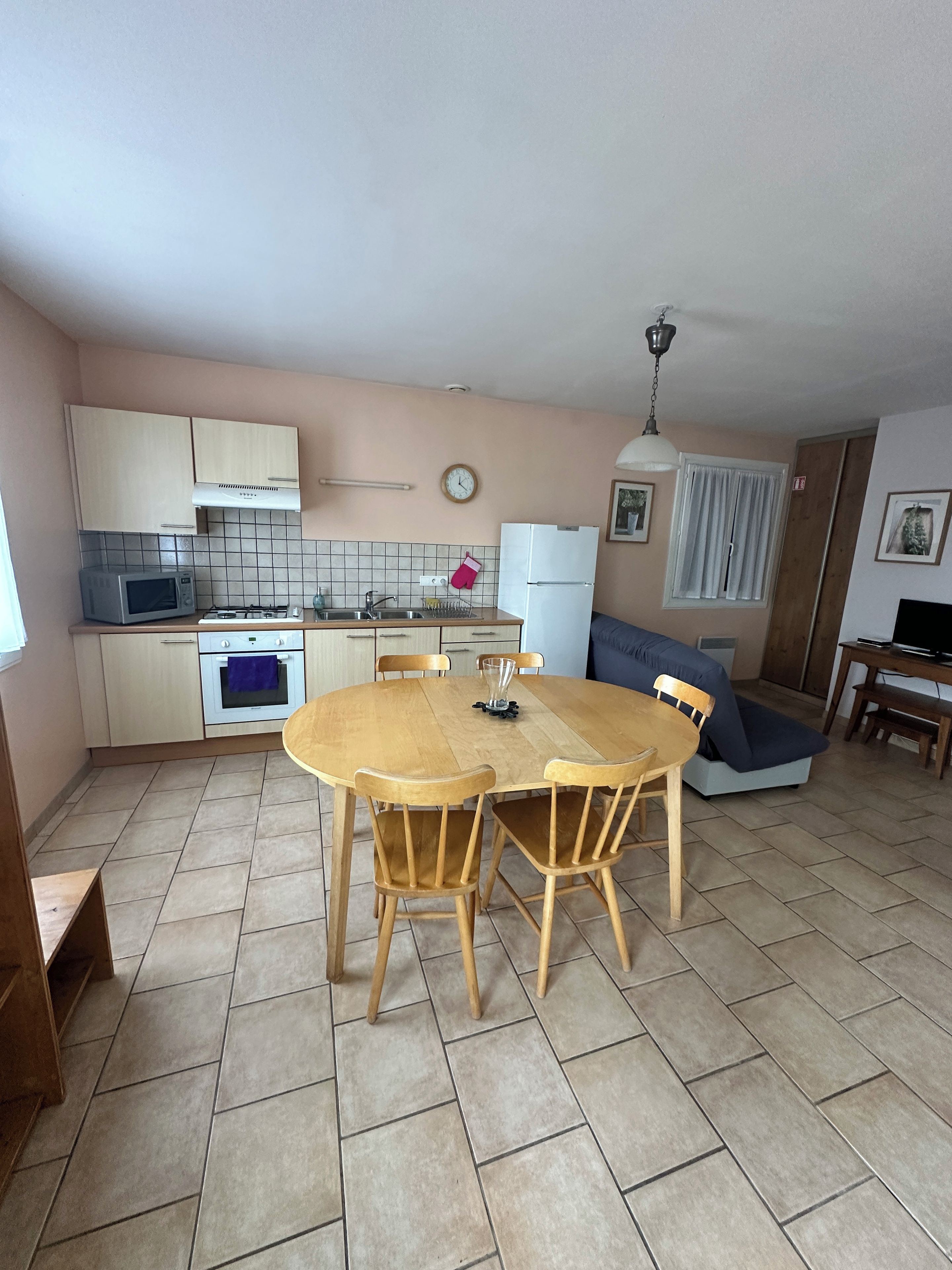 A compact kitchen with a dining table, chairs, a microwave, oven, and a refrigerator.